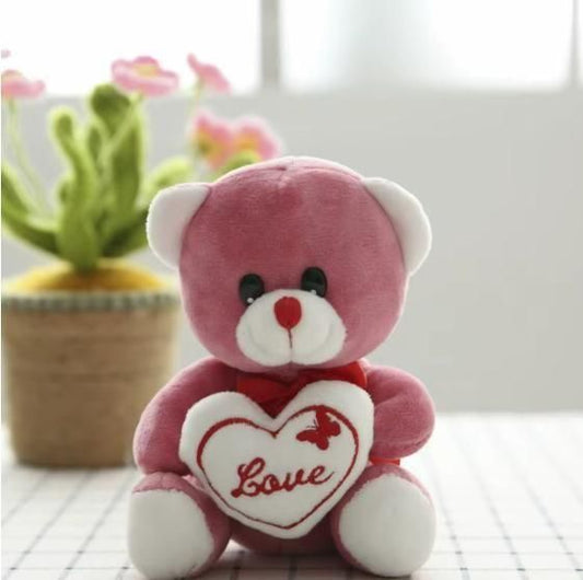 Pink teddy bear with a heart that says 'Love' on a blurred background