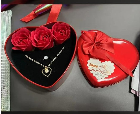 Heart-shaped jewelry box with red roses, necklace, and earrings on a gray surface.