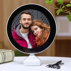 Round mirror with a photo of a couple on a stand, placed on a surface with a blurred background.